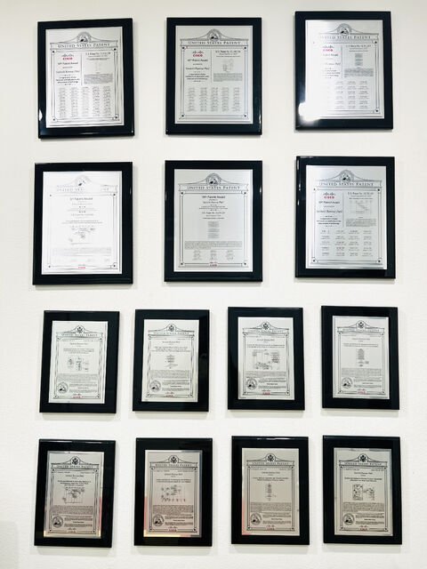 Wall of framed U.S. Patent plaques presented to Akram Sheriff at Cisco Systems
